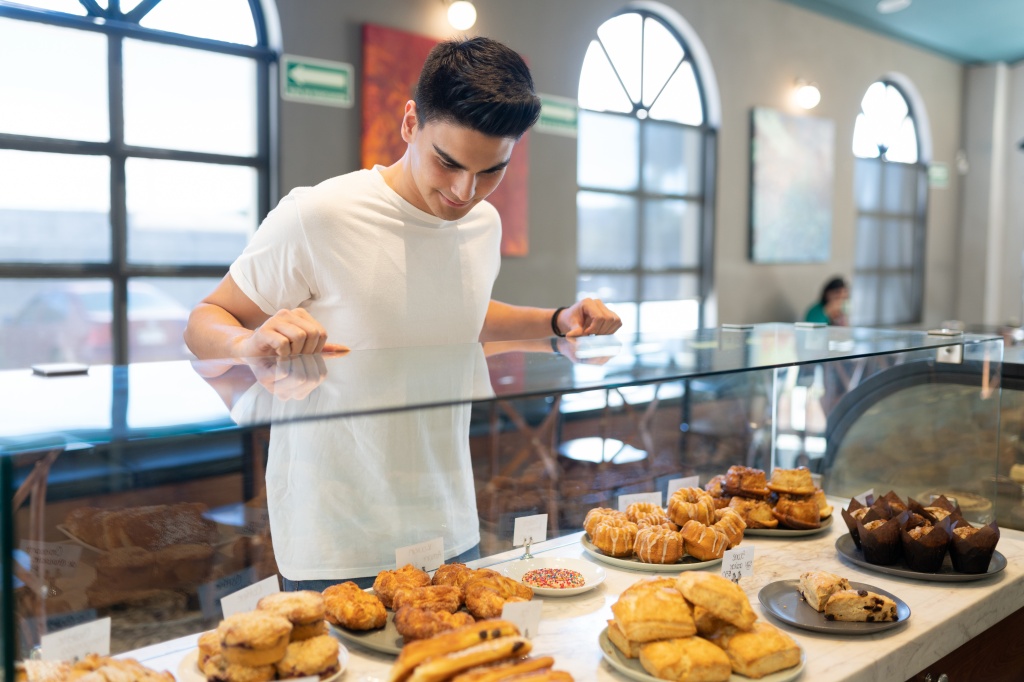 Good looking young man looking at some sweet bread and pastries in a bakery shop